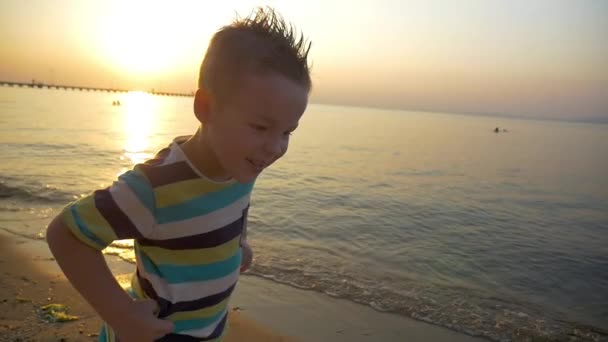 Criança fazendo rosto irritado na praia ao pôr do sol — Vídeo de Stock