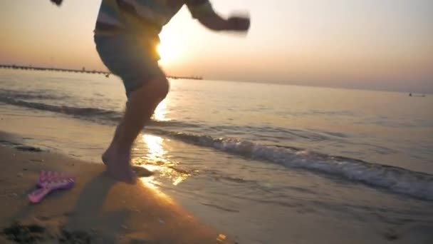 Το παιδί τρέχει ξυπόλητος κατά μήκος της θάλασσας στο ηλιοβασίλεμα — Αρχείο Βίντεο