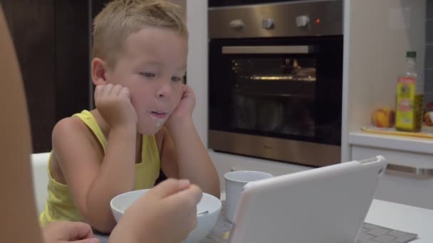 Мать кормит ребенка, пока он смотрит планшетный компьютер — стоковое видео