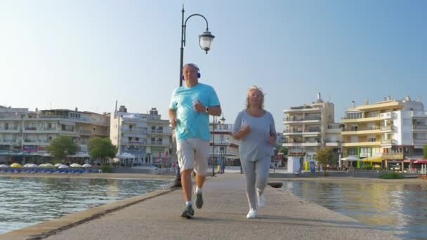 Pareja mayor trotando con música en el muelle — Vídeos de Stock