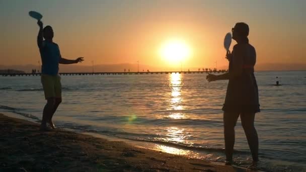 Pareja jugando al tenis en la playa al atardecer — Vídeos de Stock