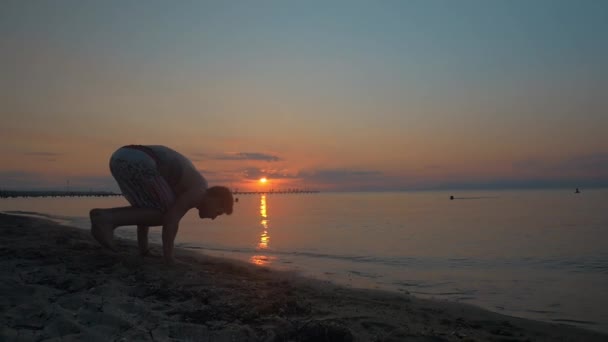 Мужчина делает стойку на руках на пляже на закате — стоковое видео