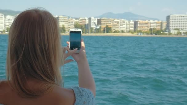 Женщина с камерой, стреляющая по морю и городу с корабля — стоковое видео