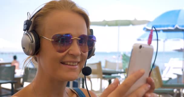 Крупним планом молода жінка в навушниках розмовляє по телефону — стокове відео