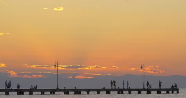 İnsanlar izlerken günbatımı pier üzerine — Stok video