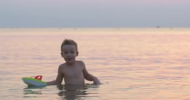 Niño jugando con juguete barco en el mar — Vídeos de Stock