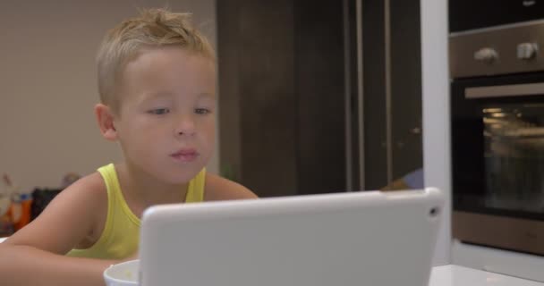 Bambino piccolo è occupato con guardare pad durante il pasto — Video Stock