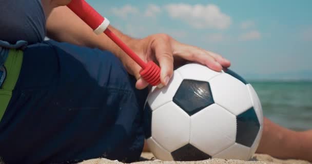 Homem bombeando uma bola de futebol na costa — Vídeo de Stock