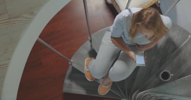 Женщина со смартфоном пьет кофе на спиральной лестнице — стоковое видео