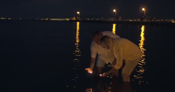 Älteres Paar lässt Kerzen nachts im Meer schwimmen — Stockvideo