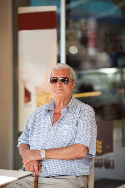 Ηλικιωμένος άνδρας σε αναμονή σε ένα τραπέζι έξω από ένα κατάστημα — Φωτογραφία Αρχείου
