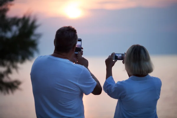 Visão traseira do casal tirando fotos do pôr do sol — Fotografia de Stock