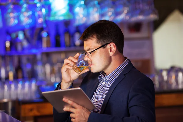 Бизнесмен с планшетом пьет виски в баре — стоковое фото