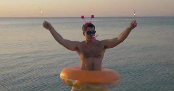 Lustiger Mann mit Gummiring und Wunderkerzen tanzt am Strand — Stockvideo