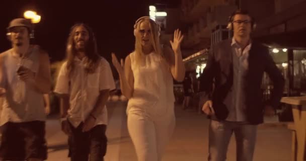 Друзья в наушниках танцуют под музыку во время ночной прогулки — стоковое видео