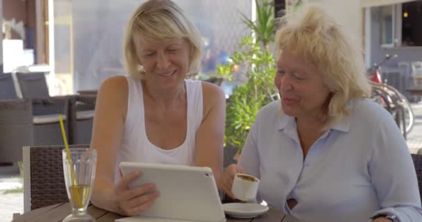 Two senior women watching photos on pad in street cafe — Stock Video