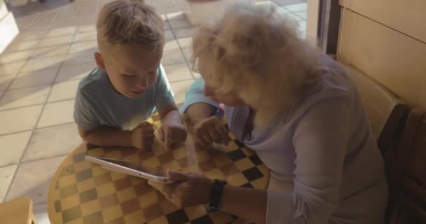 Niño y abuela entretenido con almohadilla táctil en la cafetería — Vídeo de stock