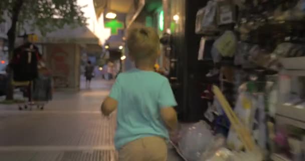 Маленький мальчик бежит по городской улице вечером — стоковое видео