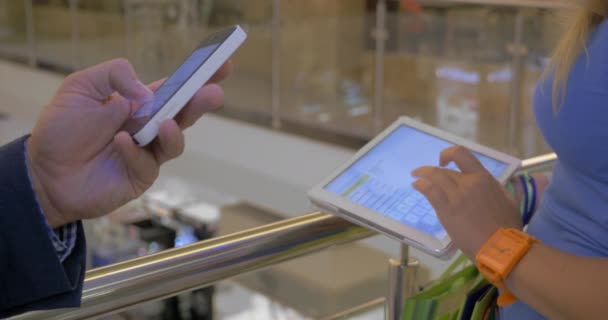 Personas que utilizan teléfonos inteligentes y almohadillas en el centro de comercio — Vídeos de Stock