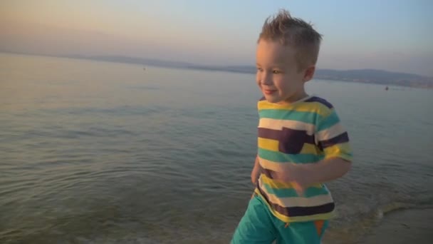 Gelukkige jongen uitgevoerd aan de kust van de zee bij zonsondergang — Stockvideo