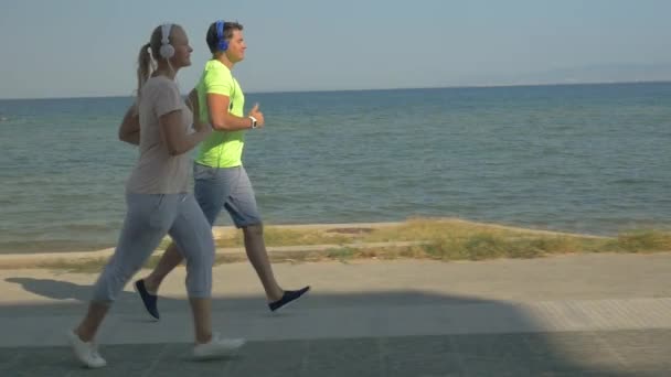 Uomo e donna che corrono sul marciapiede vicino al mare — Video Stock