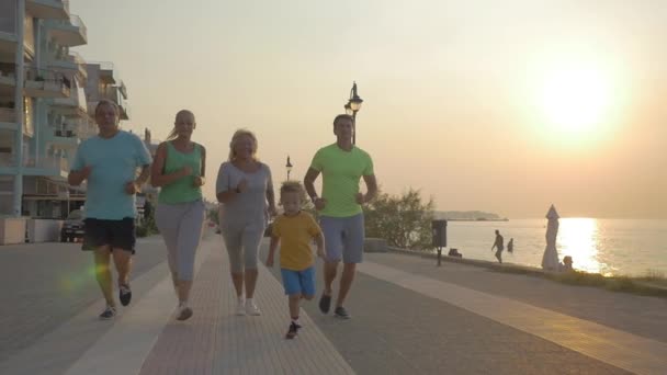 Дружня сім'я біжить до кінця на тротуарі на заході сонця — стокове відео