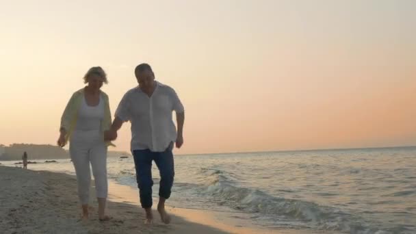 Senior couple running on the beach at sunset
