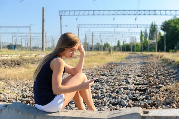Teenager-Mädchen mit Handy sitzt auf unfertigem Bahngleis — Stockfoto