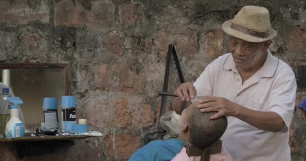 Hombre mayor afeitando a otro hombre por hoja vieja, corte de pelo tradicional — Vídeo de stock