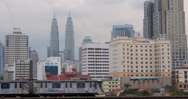 En tren pasa tren. En el fondo visto Petronas Twin Towers, hotel y rascacielos — Vídeos de Stock