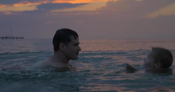 Στο ηλιοβασίλεμα πατέρα με τον γιο, κολύμπι στη θάλασσα της πόλης Περαία, Ελλάδα — Αρχείο Βίντεο