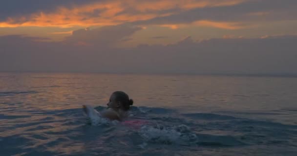 Young woman swims away in the sea at sunset, magical view of evening cloudy sky and calm sea — Stock video