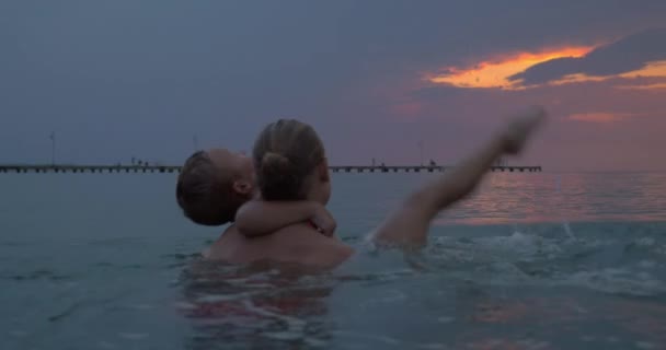 Au coucher du soleil mère avec son fils nageant dans la mer de la ville Perea, Grèce — Video