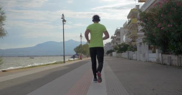 Joven con auriculares corre por la carretera de la ciudad Perea, Grecia — Vídeo de stock