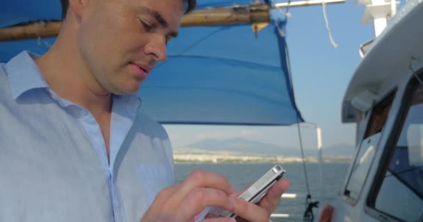 Mann tippt auf seinem Smartphone, während er an einem sonnigen Sommertag auf dem Boot segelt — Stockvideo