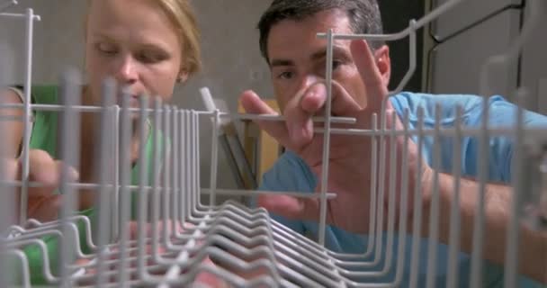 Молода пара відкриває посудомийну машину і завантажує туди посуд — стокове відео