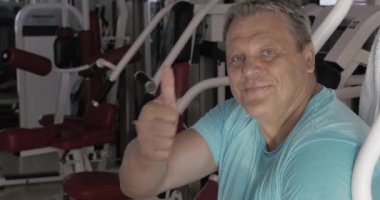Spor salonunda egzersizleri arasında başparmak ve gülümseme ile Kıdemli adam