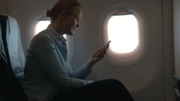 Dans la cabine de la fille de l'avion assis sur la chaise et en utilisant le terminal mobile sur le téléphone et paie pour l'achat par carte — Video