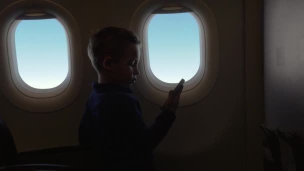 En cabina de avión niño sosteniendo un teléfono y viendo un video — Vídeos de Stock