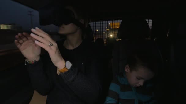 En Nea Kallikratia, Grecia en coche monta una joven madre con gafas de realidad virtual y cerca de sentarse a su pequeño hijo — Vídeos de Stock