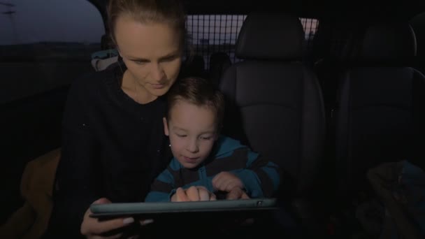 In Nea Kallikratia, Greece in car rides mother with a young son, who plays on the tablet — Stock Video