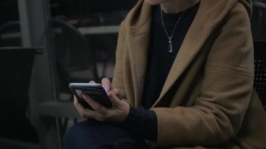 Bir cep telefonu tutan genç kız bir sandalyede oturur