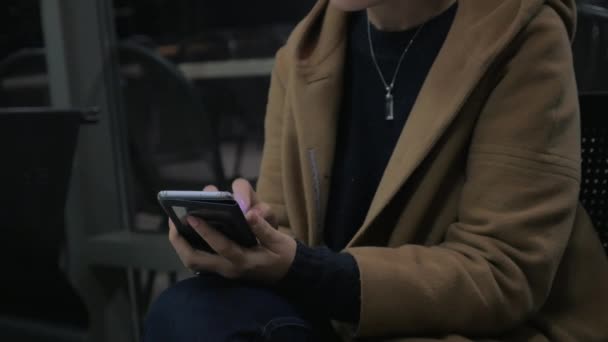 Молодая девушка сидит на стуле, держа мобильный телефон — стоковое видео