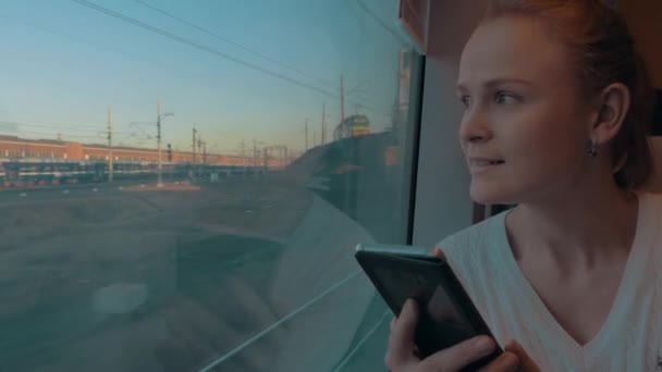 ロシアのサンクトペテルブルクでは、電車の中で若い女の子に乗って窓の外を見て、携帯電話を持っています — ストック動画