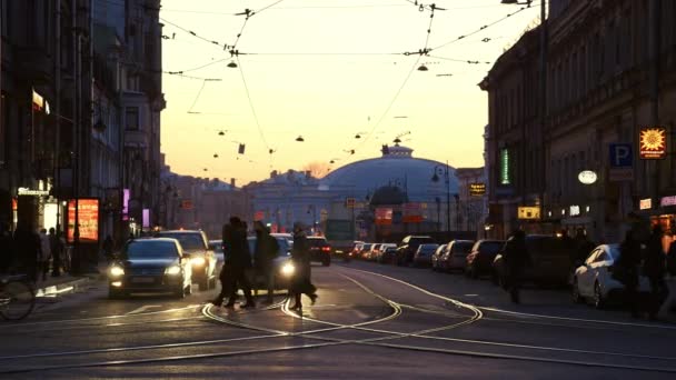 Al atardecer en la intersección personas cruzando la carretera, pasando coches — Vídeos de Stock