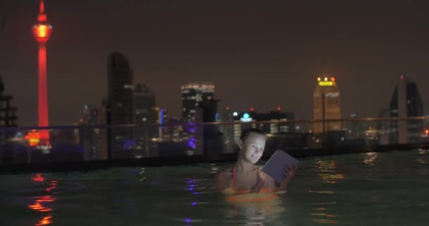 In piscina sul tetto di un hotel a Kuala Lumpur, Malesia sta nuotando giovane ragazza e lavora su tablet — Video Stock