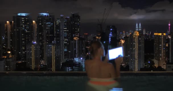 高層ビルの屋根と夜の風景には、スイミング プールでのタブレットでノートを取る女性の眺め。クアラルンプール、マレーシア — ストック動画