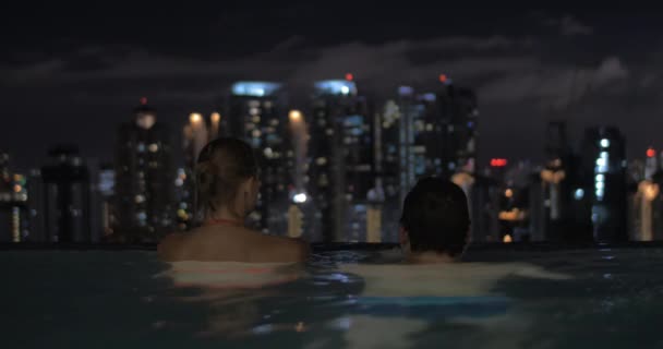 Görünüm havuzun içinde kadın gökdelenin çatı ve ardından yüzme adam onun hakkında gece şehir manzarası. Kuala Lumpur, Malezya — Stok video