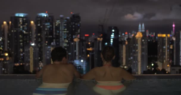 En la piscina en el techo de un hotel en Kuala Lumpur, Malasia hombre con mujer mirando a la ciudad de la noche — Vídeo de stock