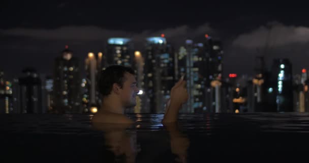 Ansicht des Mannes im Schwimmbad auf dem Wolkenkratzer-Dach mit Tablet gegen nächtliche Stadtlandschaft. kuala lumpur, malaysien — Stockvideo